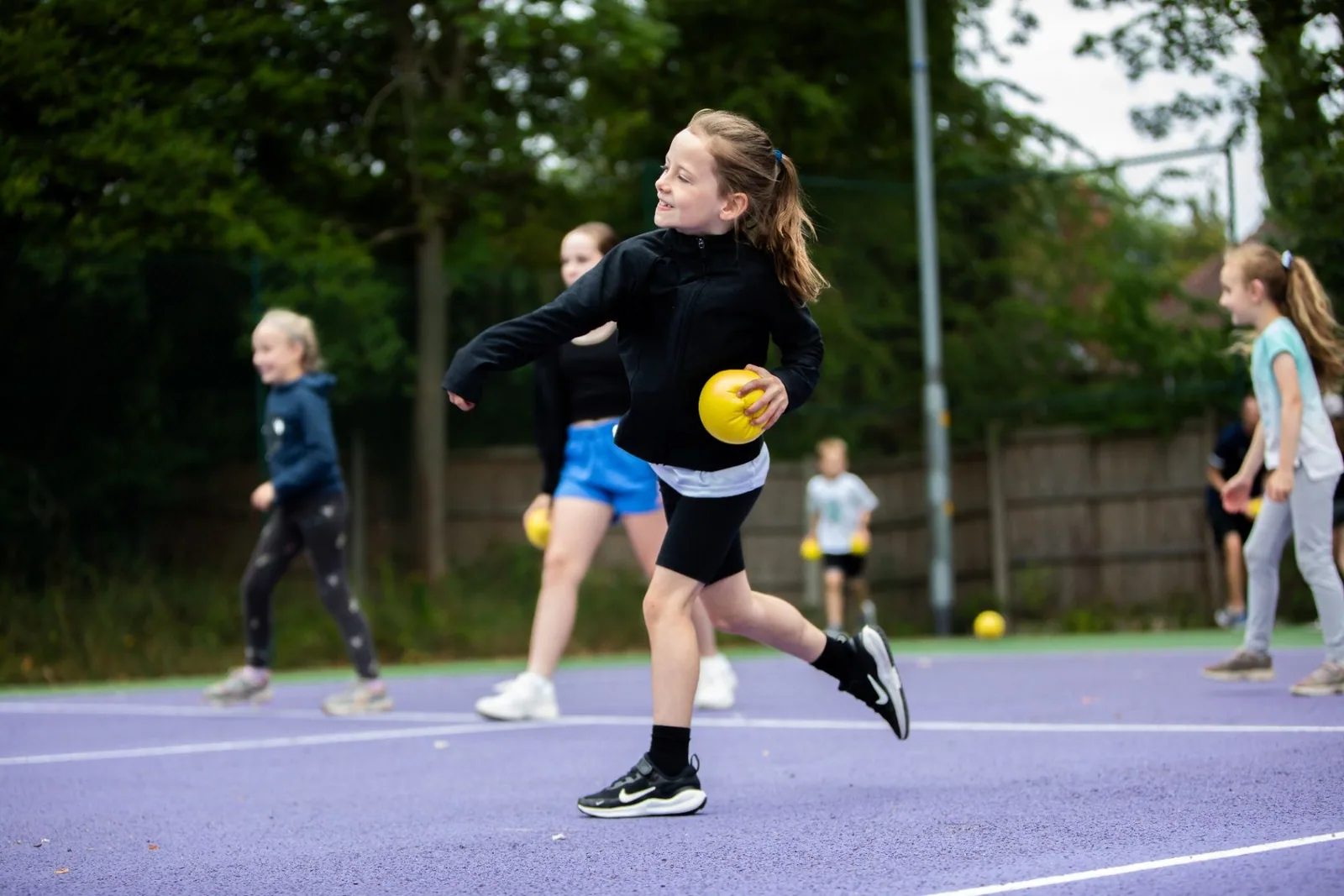 Young player running with a yellow ball on an outdoor court