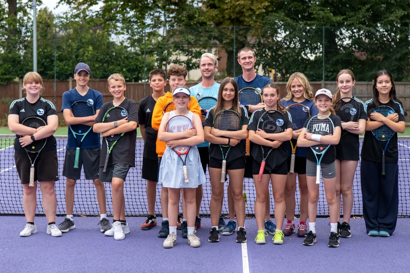 The MH Tennis coaching team and young players standing together on a tennis court